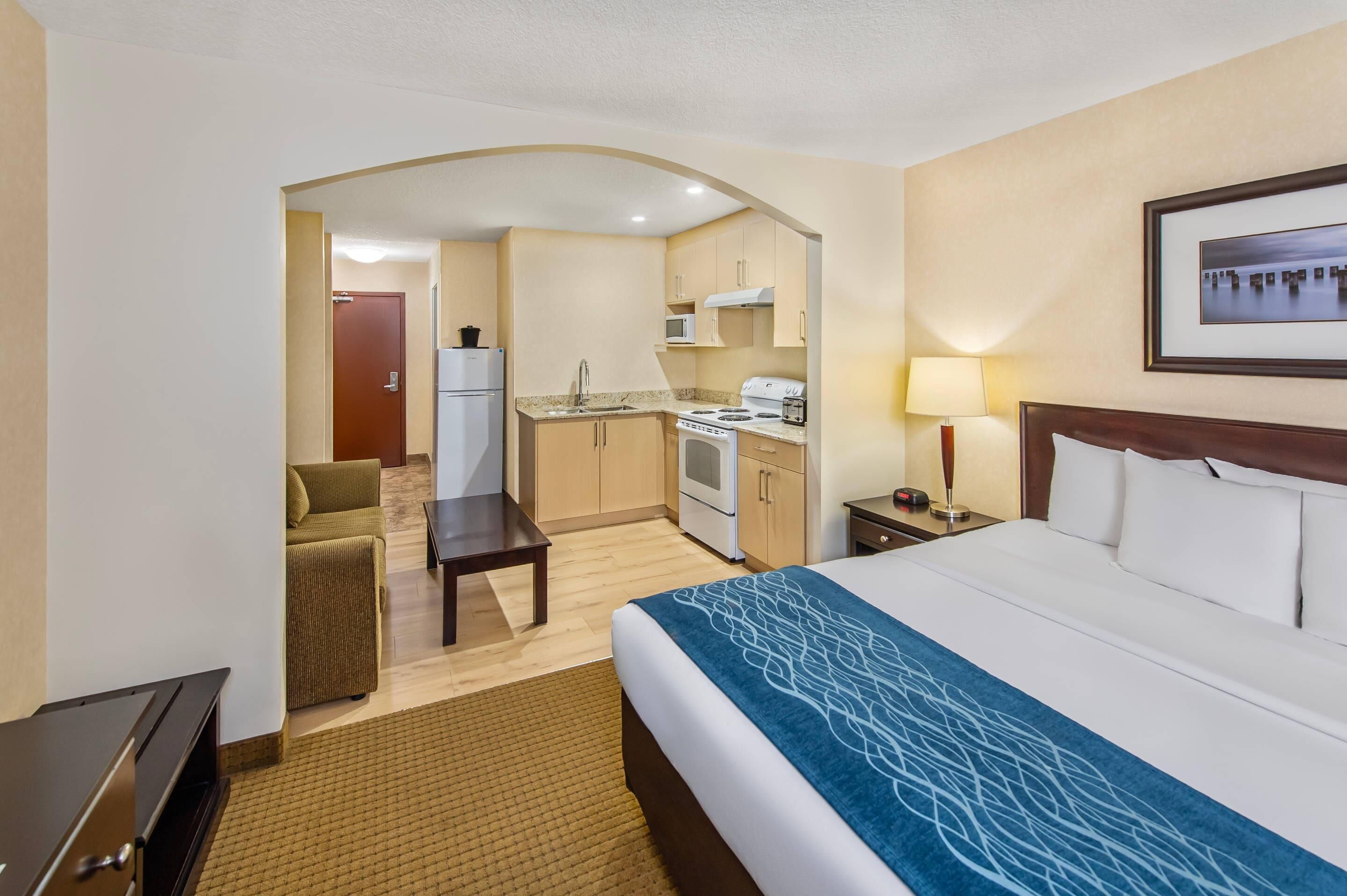 A hotel room with a bed, a desk, a kitchenette, and a living area.