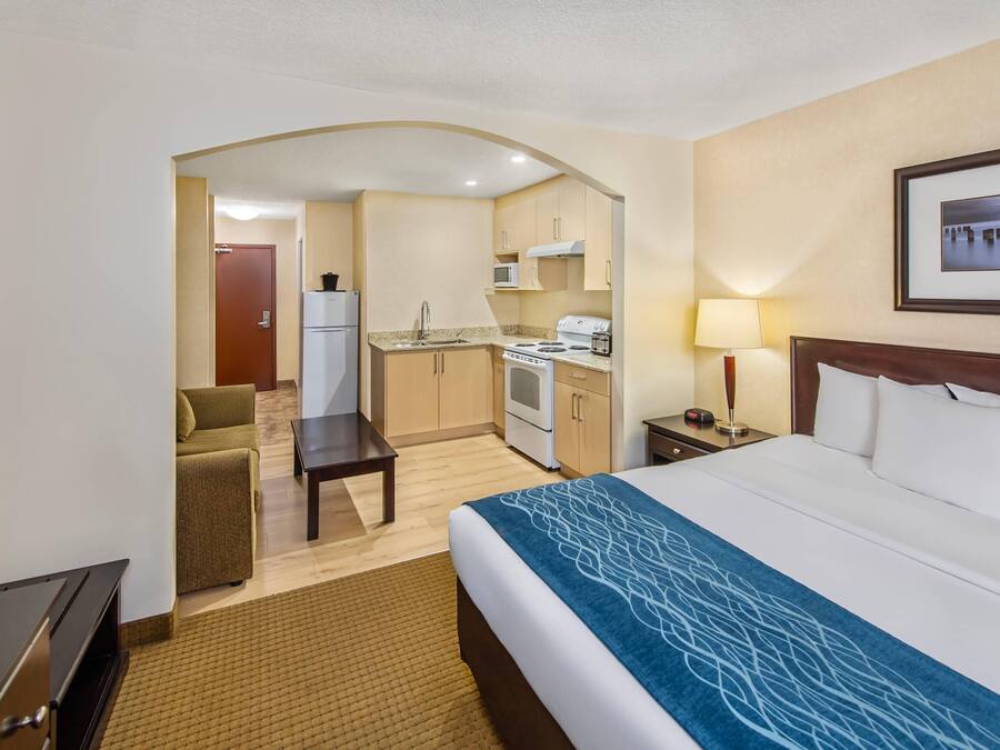A hotel room with a bed, a desk, a kitchenette, and a living area.