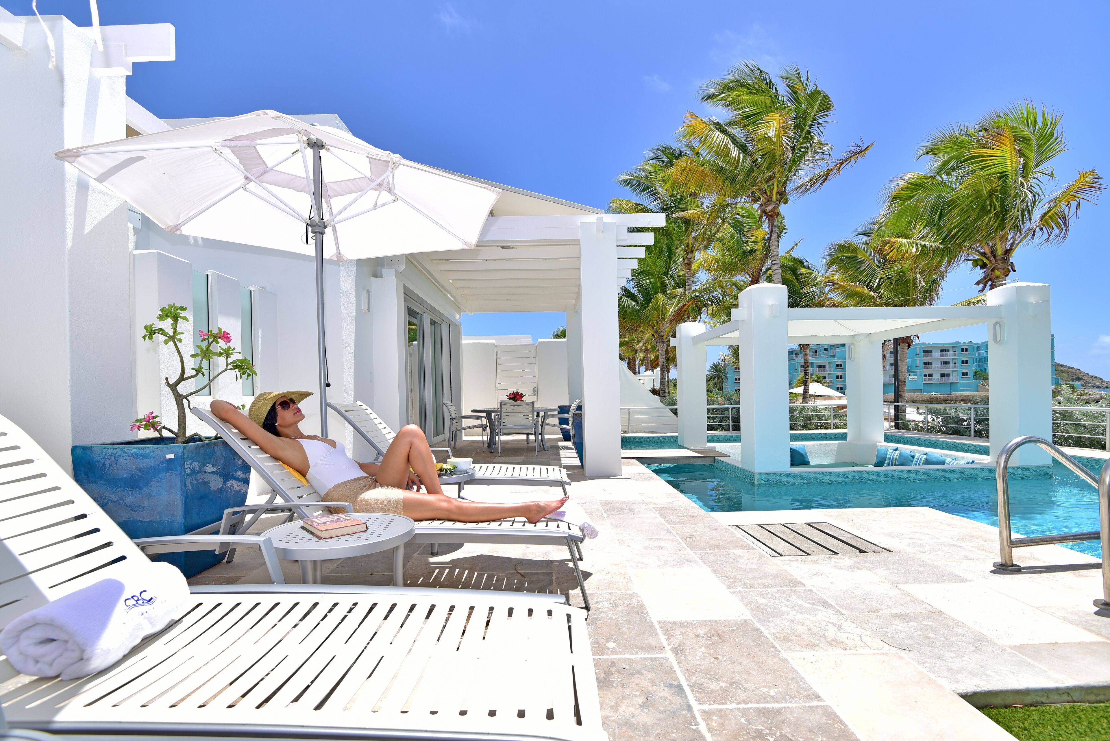 A poolside area with lounge chairs, a pool, and palm trees.