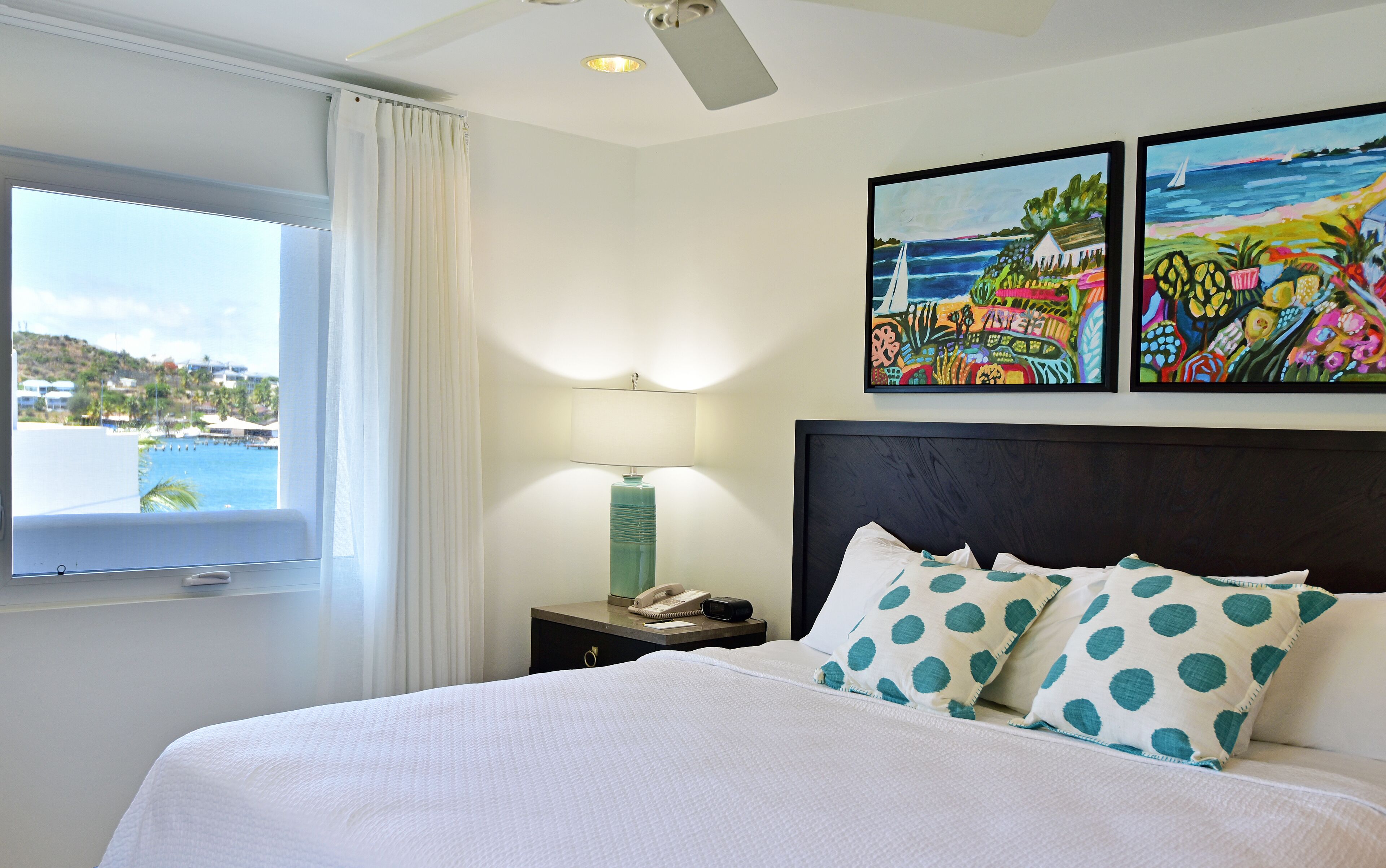 A hotel room with a bed, a nightstand, a lamp, and two paintings on the wall.