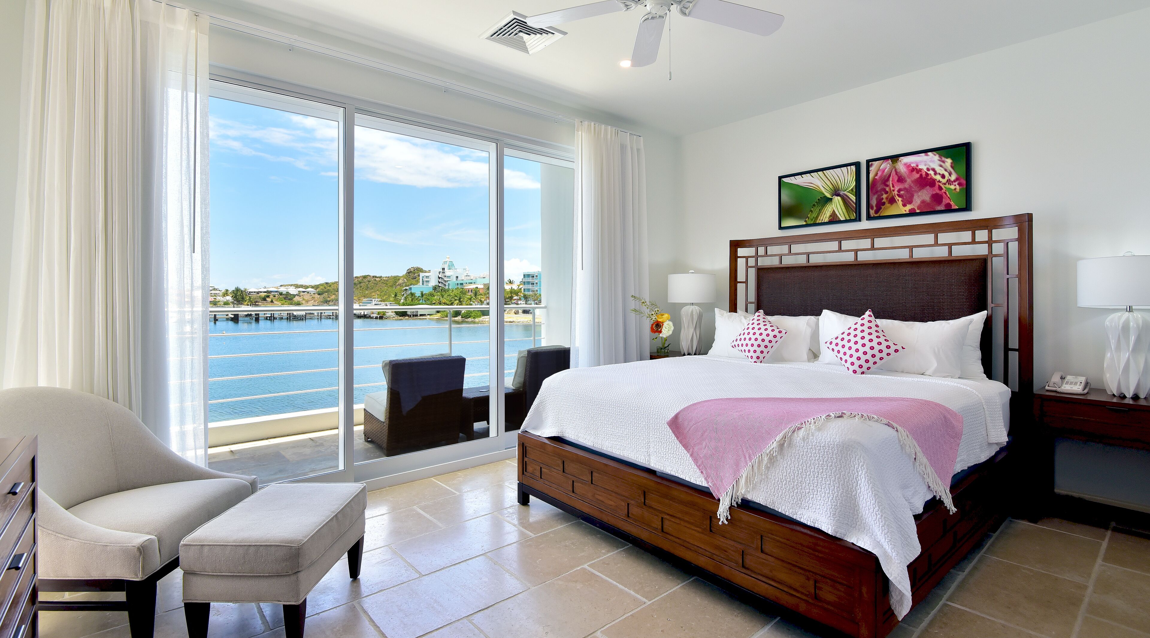 A hotel room with a large bed, a chair, a desk, and a view of the water.
