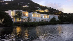 Propiedad frente al agua con varias edificaciones, una palmera y un cuerpo de agua que refleja luces.