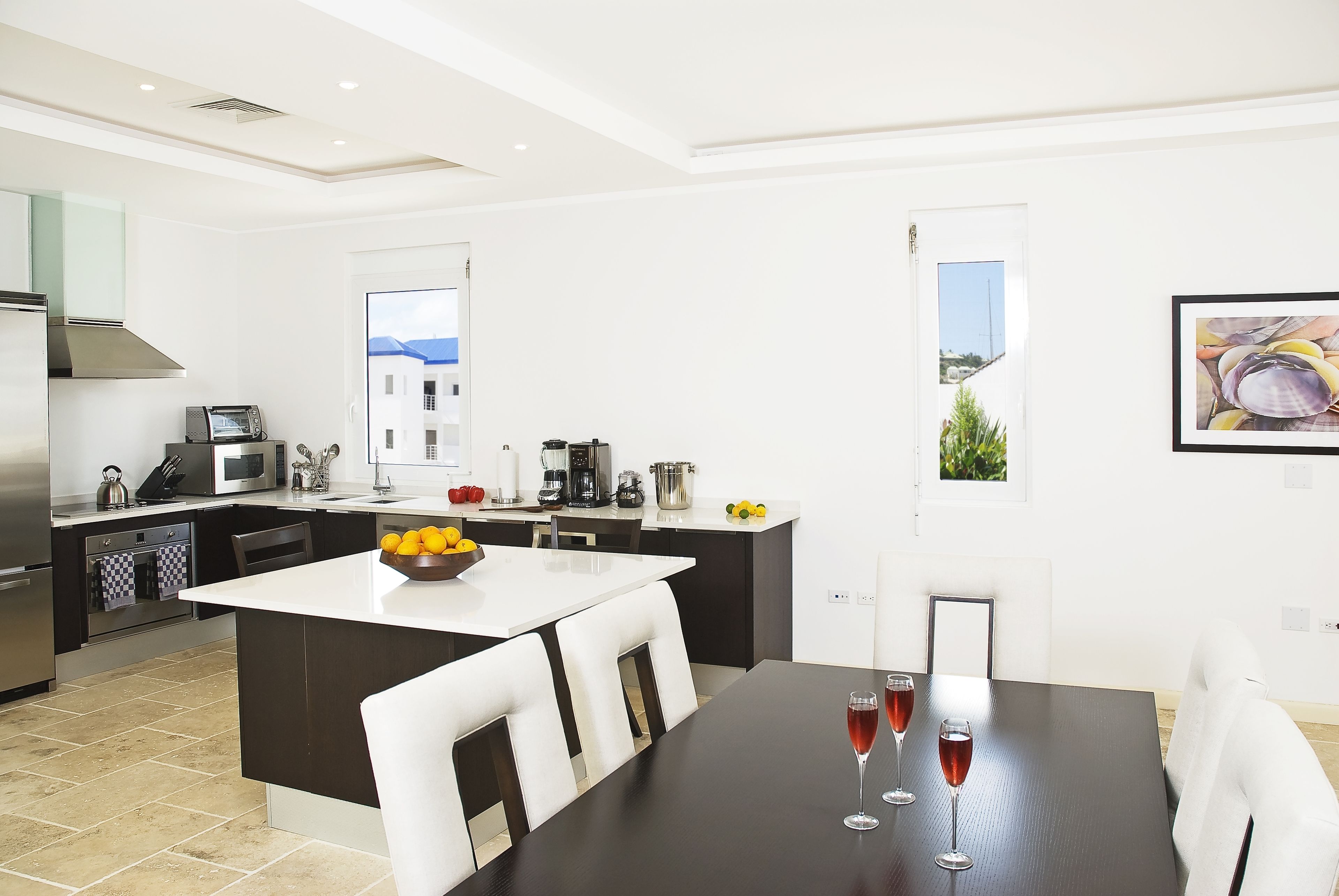A modern kitchen with a central island, white chairs, and a dining table with two glasses of red wine.