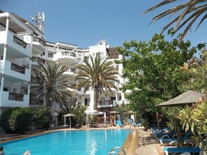 Un hotel con piscina, palmeras y un cielo azul despejado.