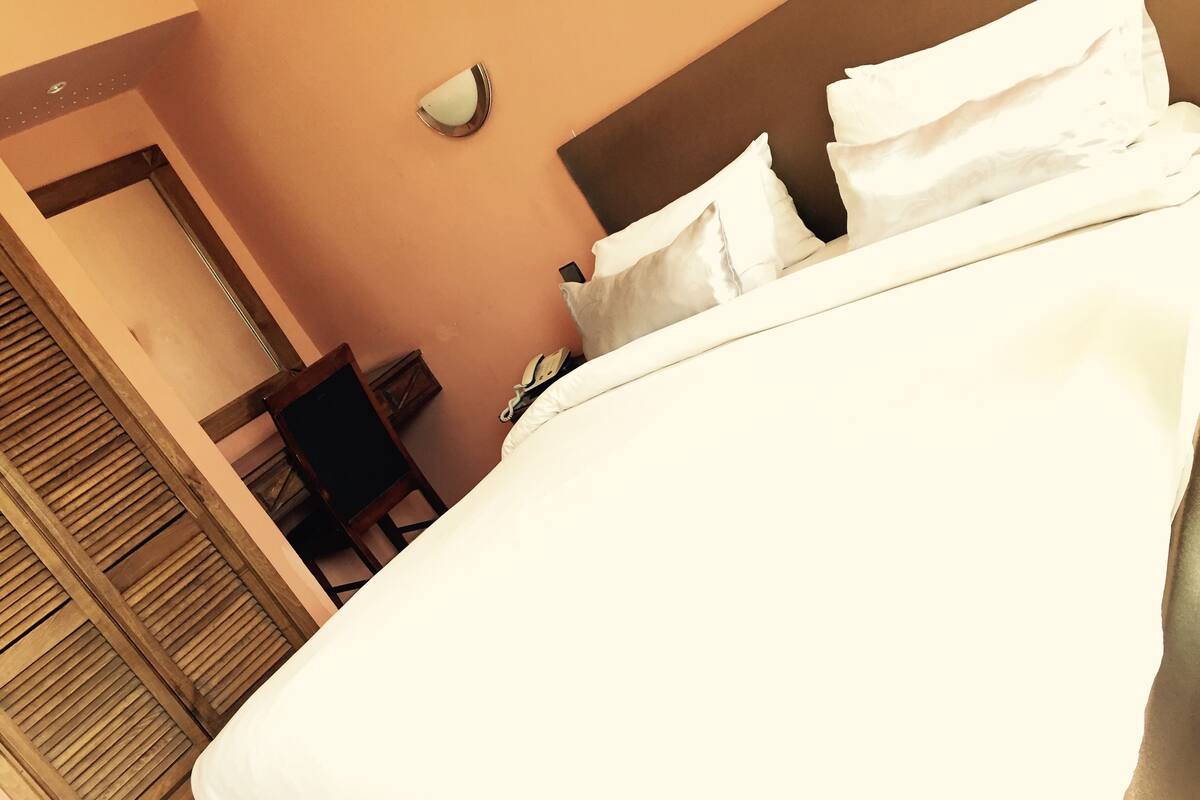 A bedroom with a bed, a chair, a bedside table, and a wall-mounted light fixture.