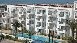A multi-story hotel with balconies, a swimming pool, and a view of the sea. - Flathotel (Agadir)