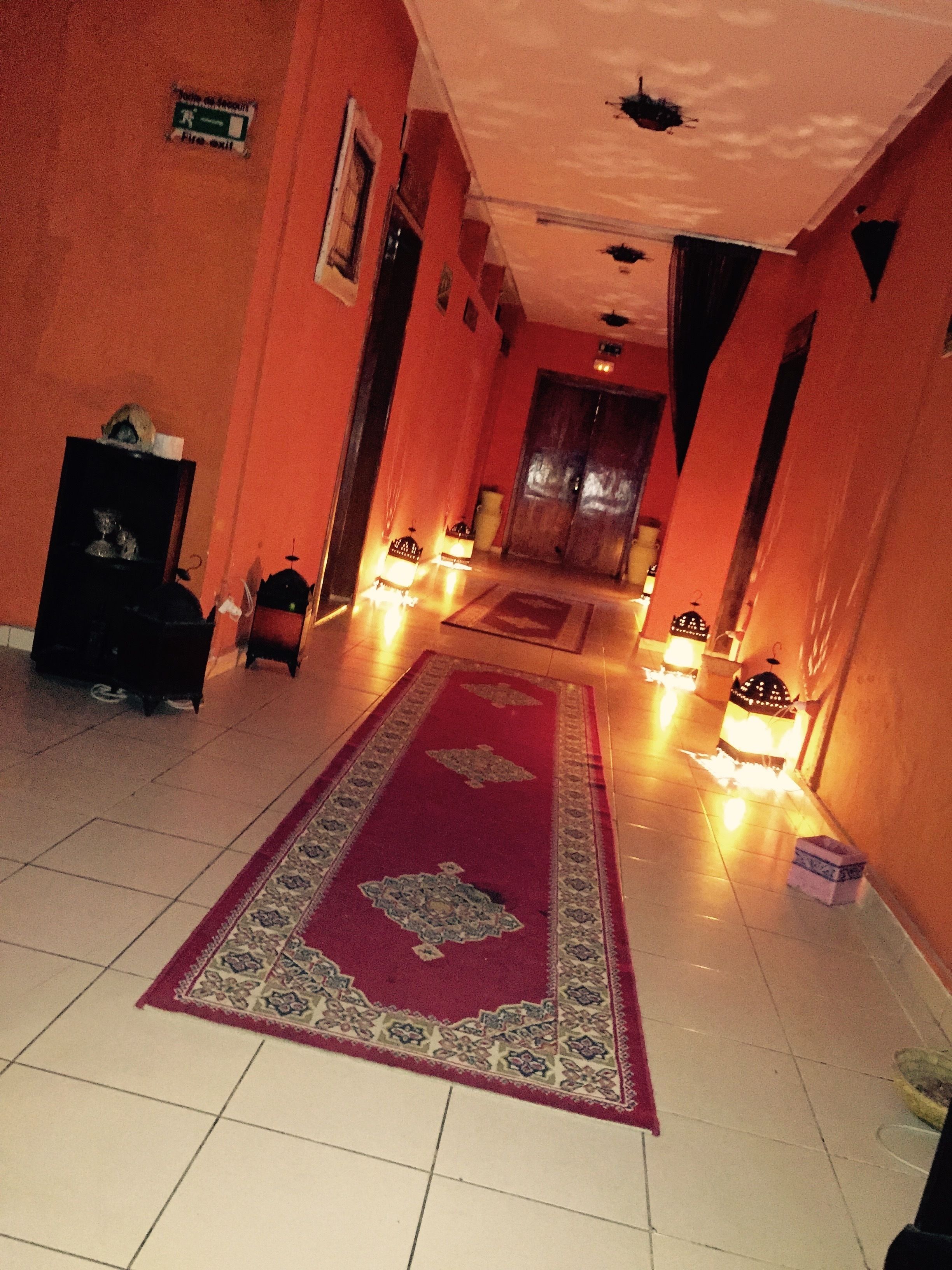 Un pasillo con alfombra roja, suelo de baldosas y luces fijadas en la pared.