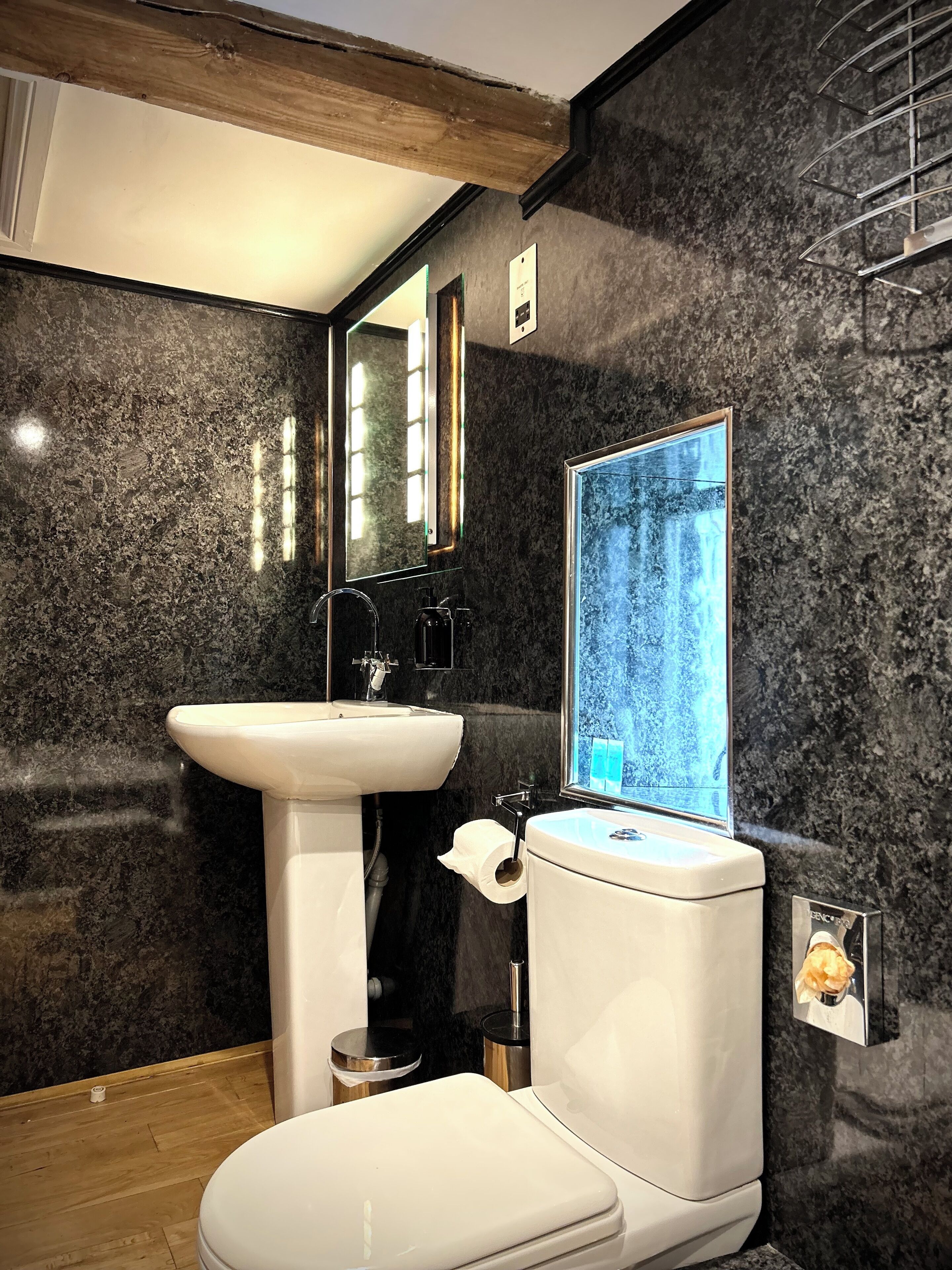 Une salle de bain moderne avec un lavabo, des toilettes et un miroir, le tout de couleur blanche. Les murs sont recouverts de marbre foncé, et une fenêtre offre une vue sur les arbres.