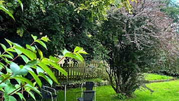 A grassy outdoor area with two metal chairs and a wooden fence.