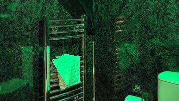 Un baño con una ducha iluminada en verde, un inodoro y un cubo de basura.