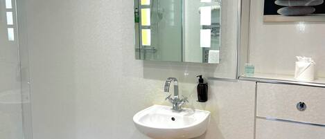 Un baño moderno con cabina de ducha de vidrio, lavamanos pedestal, inodoro y espejo con iluminación.
