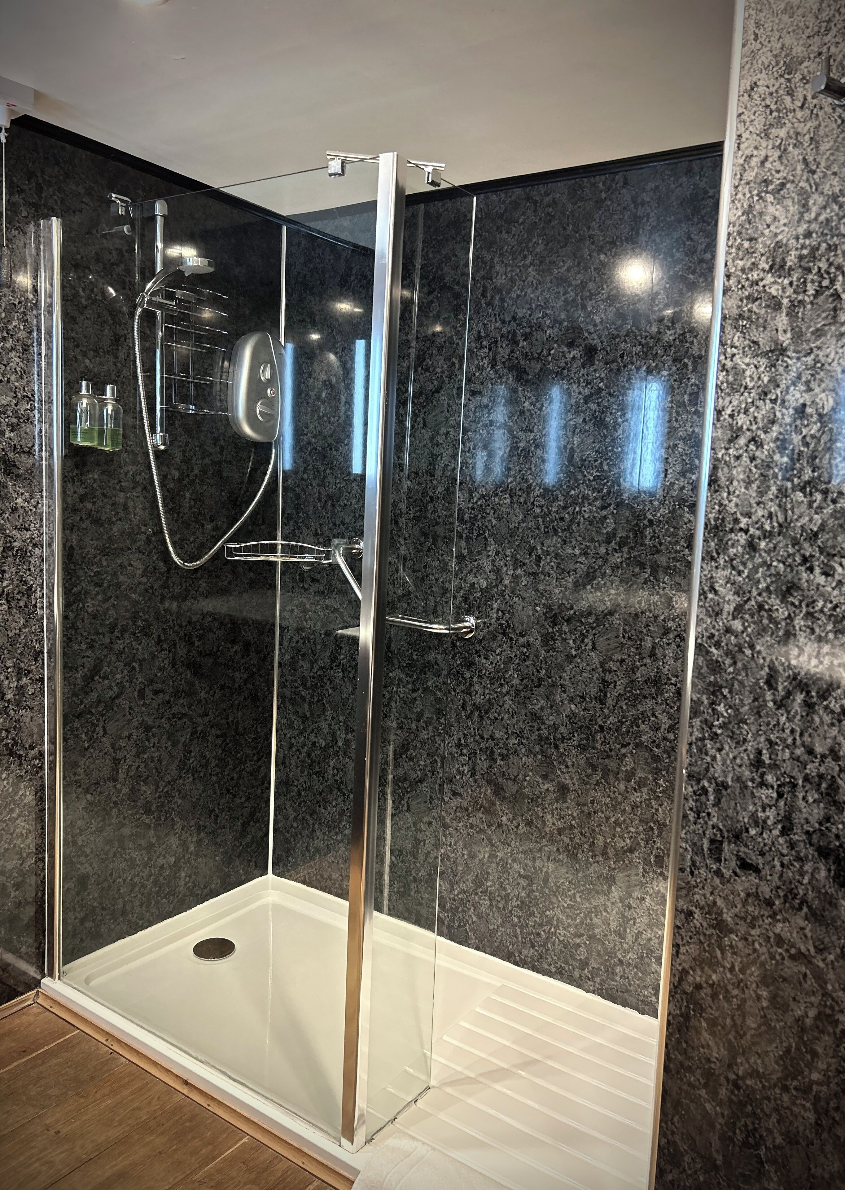 A glass-enclosed shower with a granite wall, a showerhead, and a handheld shower attachment.