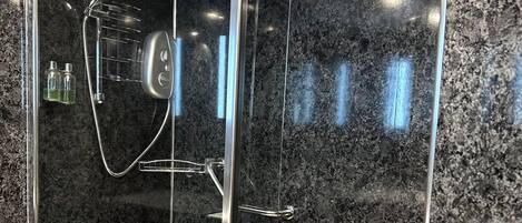 A glass-enclosed shower with a granite wall, a showerhead, and a handheld shower attachment.