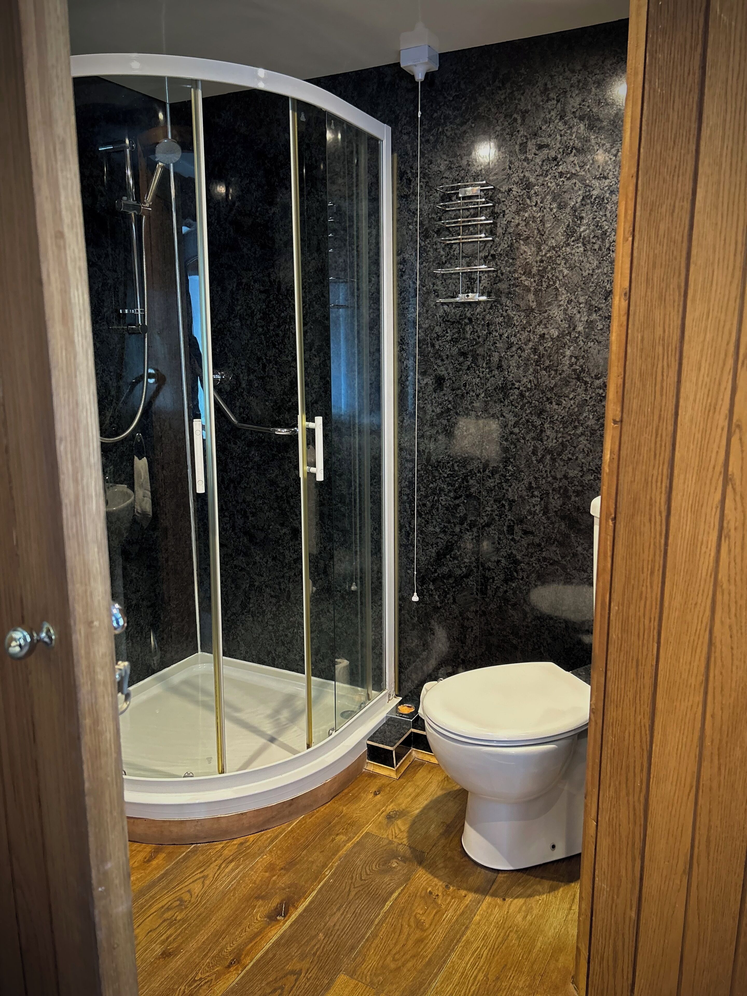 Een moderne badkamer met een douchecabine van glas, een toilet en een houten vloer.