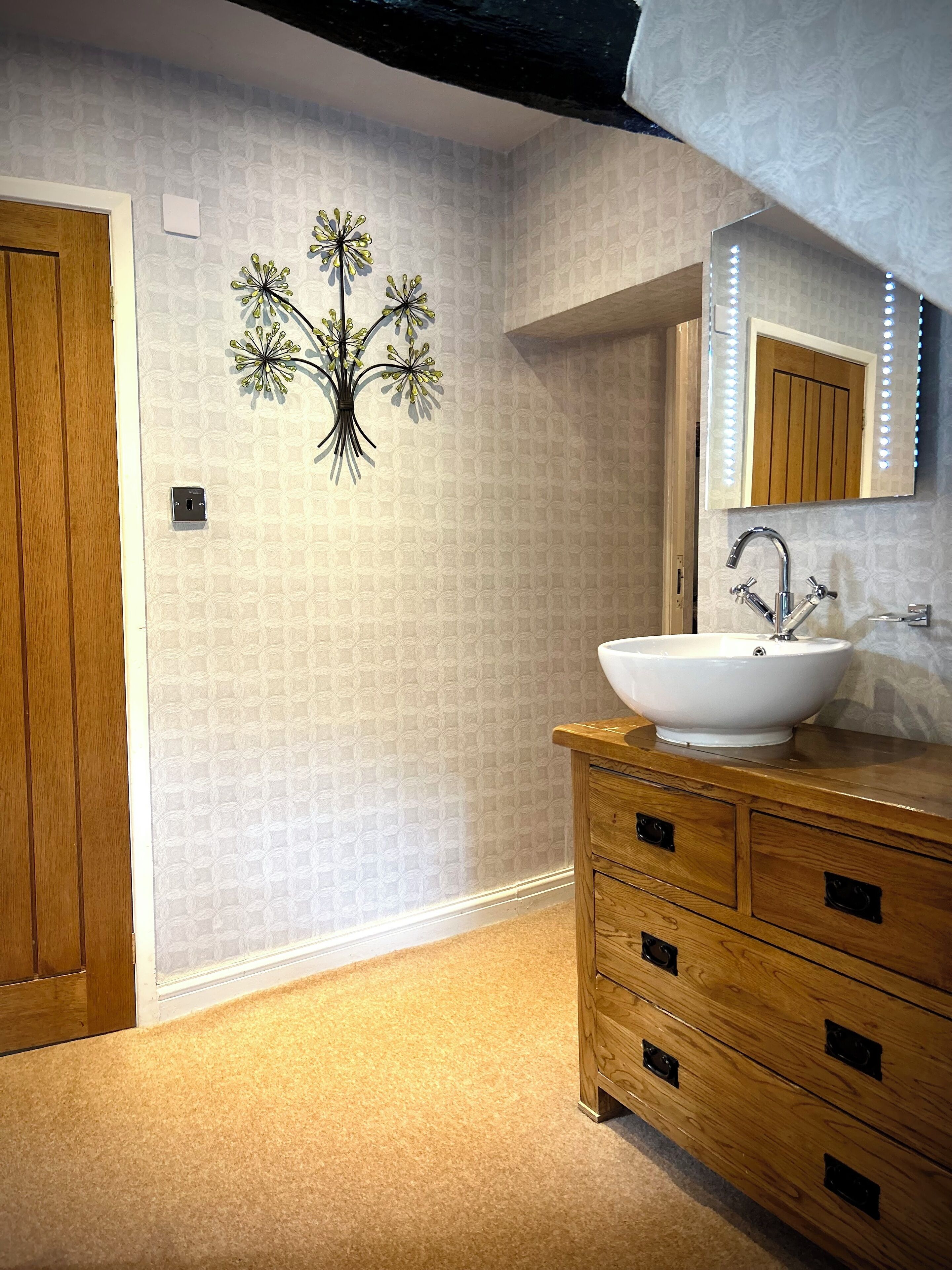 Un baño con tocador de madera, un lavabo blanco y un espejo con iluminación.