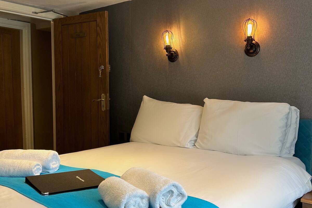 A hotel room with a bed, two wall-mounted light fixtures, a wooden door, and a blue towel on the bed.