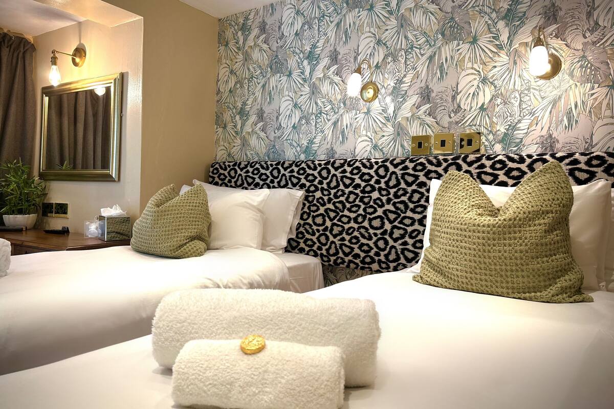 A hotel room with two beds, a leopard print headboard, a large mirror, and a tropical leaf wallpaper.