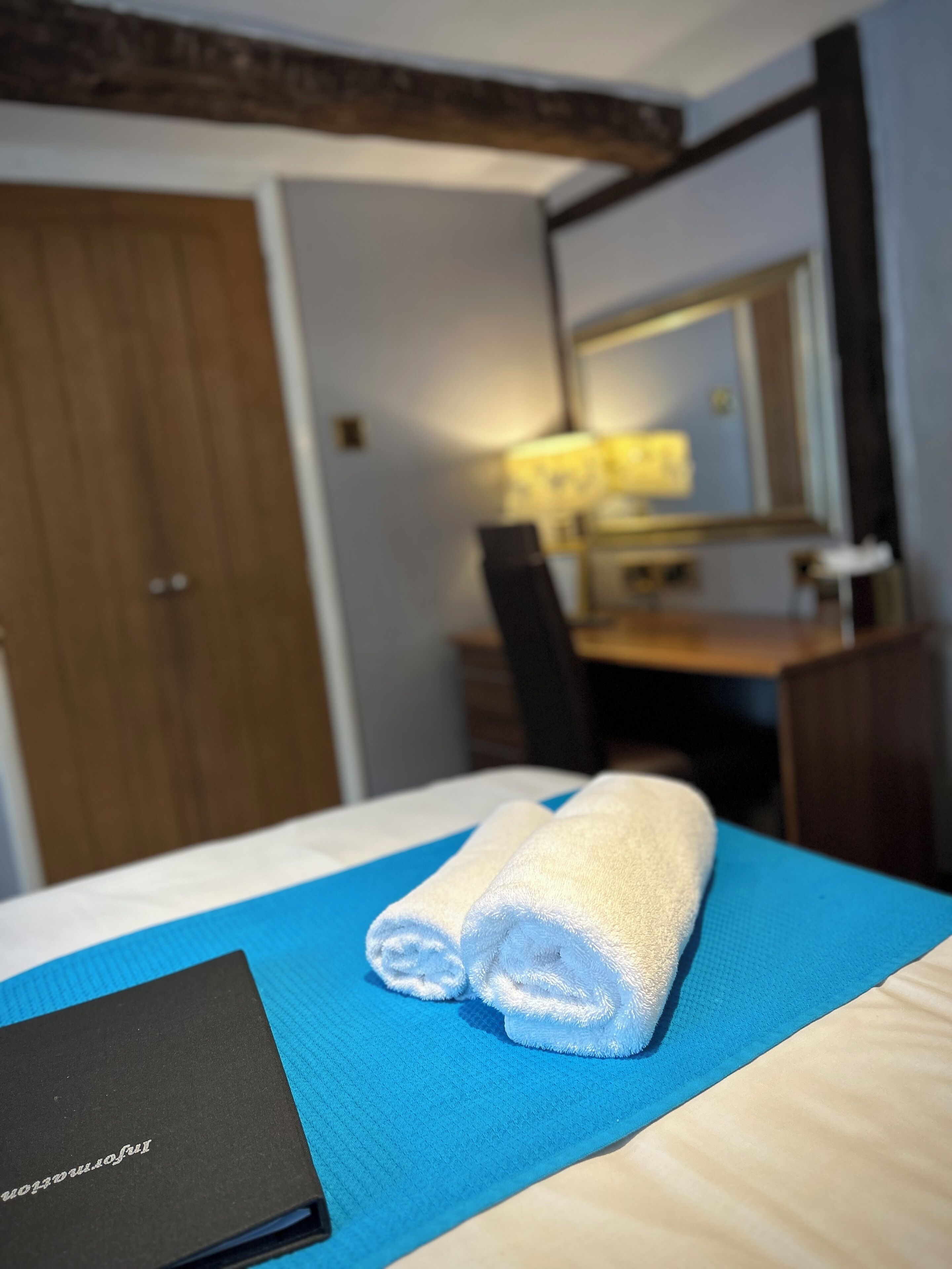 A hotel room with a bed, a desk, a chair, a lamp, and a wooden door.