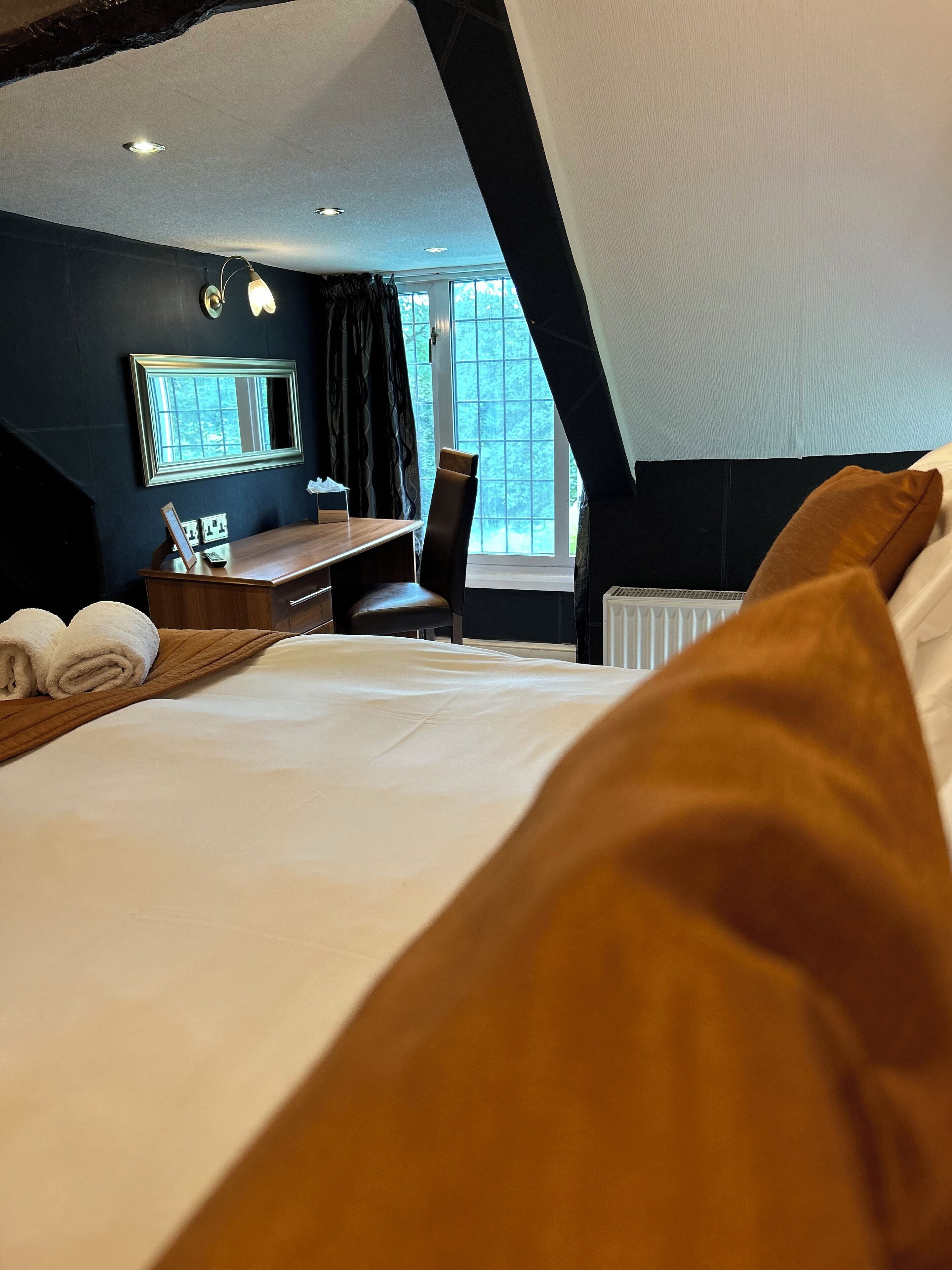 Ein Hotelzimmer mit Bett, Schreibtisch, Stuhl, Fenster und Heizkörper.