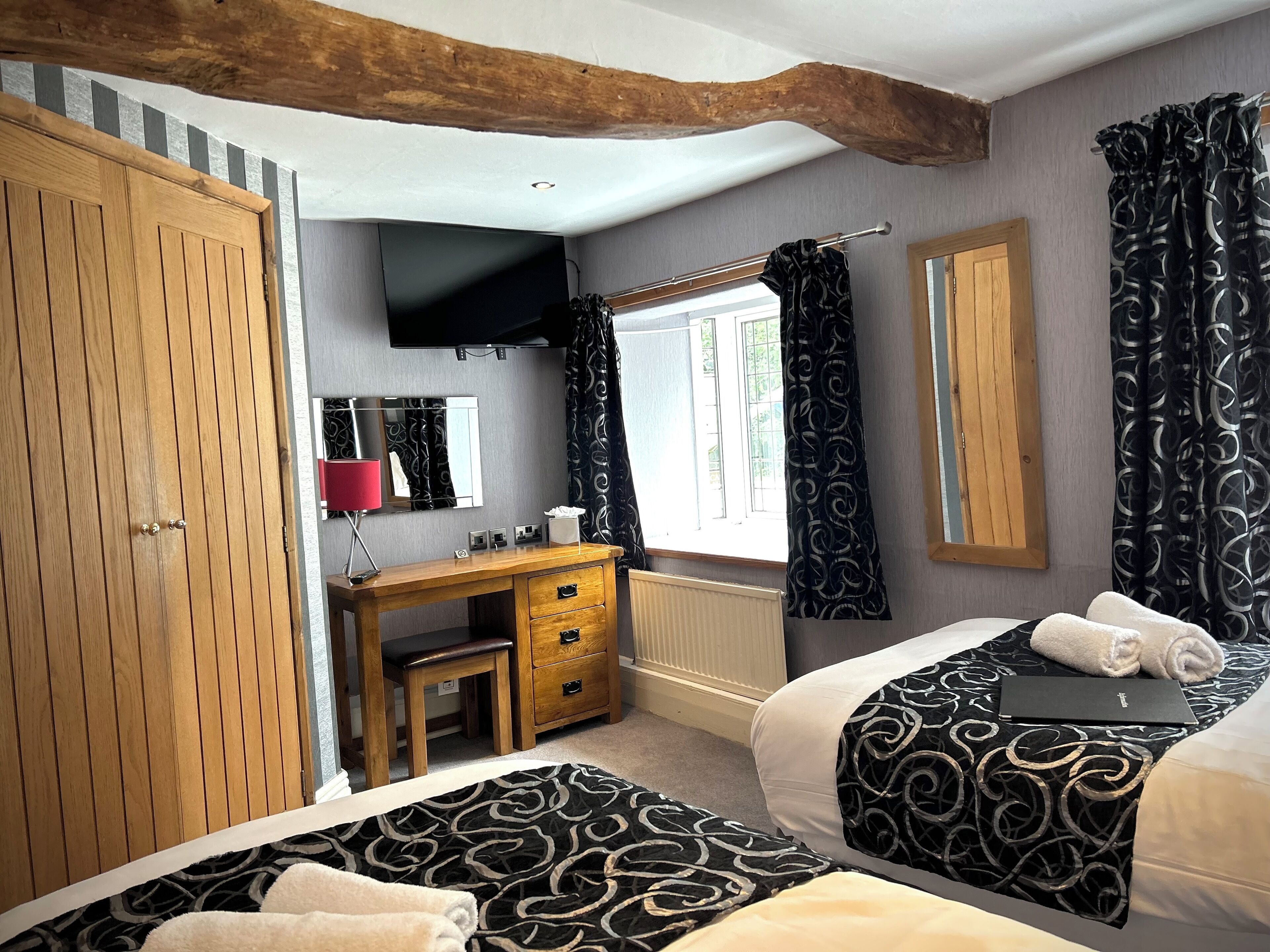 Une chambre avec une armoire en bois, un bureau avec un miroir, une télévision et deux lits avec une literie à motifs.