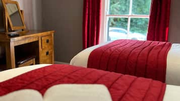 Quarto com duas camas, penteadeira de madeira, espelho e janela com cortinas vermelhas.