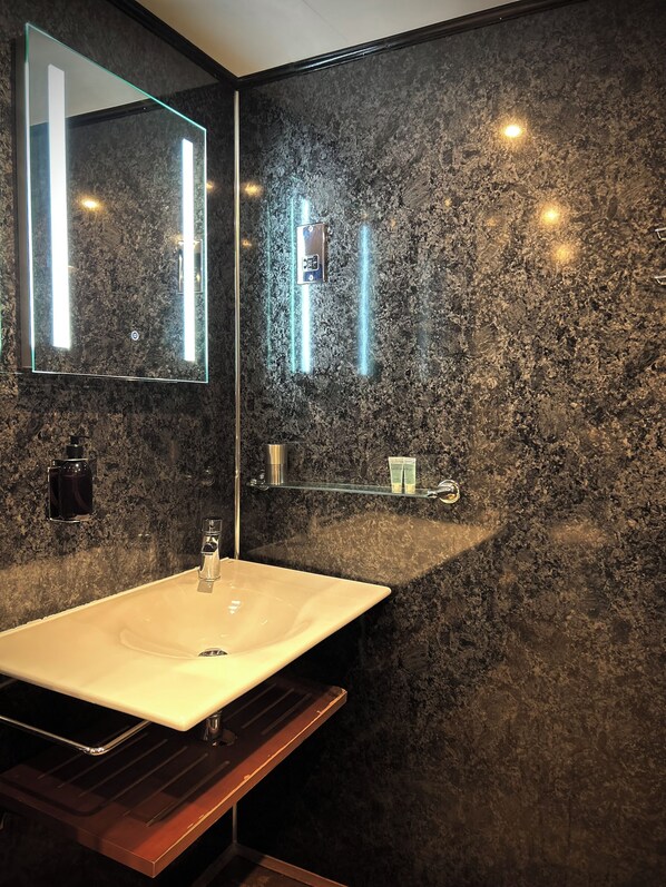 Un baño moderno con un espejo grande, un lavabo y una pared de mármol.