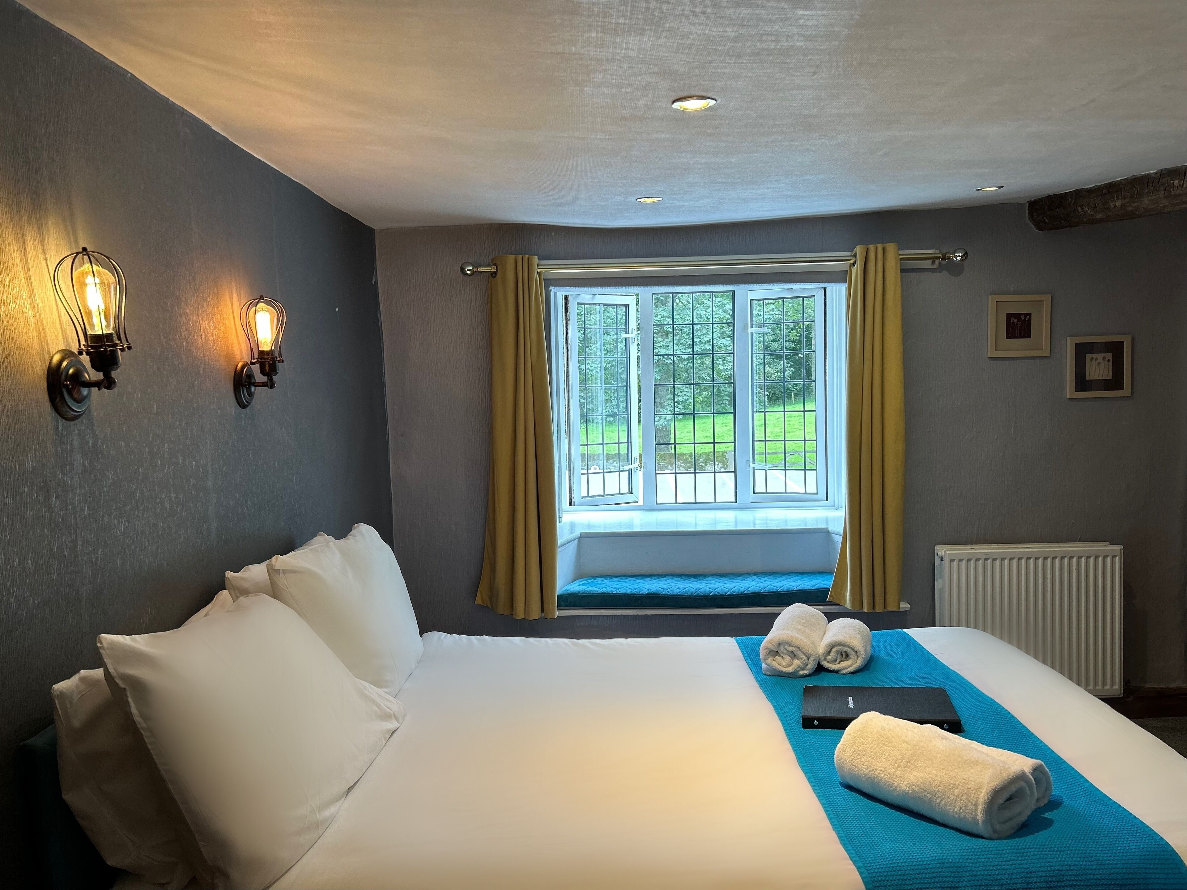 Habitación de hotel con una cama grande, dos lámparas de pared, una ventana con cortinas y un radiador.