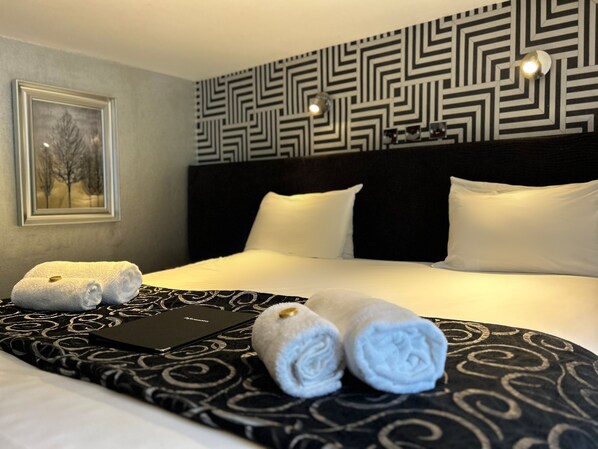 A neatly made bed with a black and white patterned bedspread, white pillows, and two rolled towels on the side. - Royal Oak Appleby (Appleby-in-Westmorland)