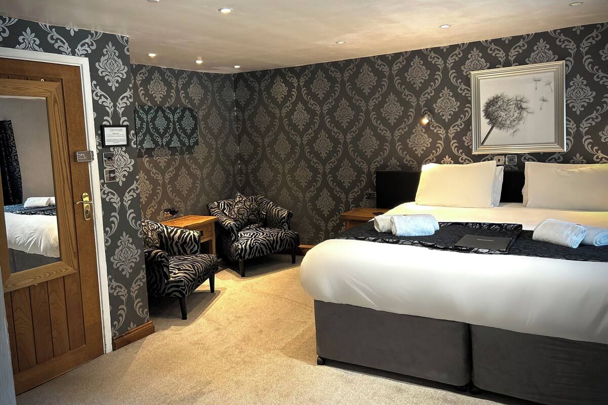 A hotel room with a bed, a zebra-patterned armchair, a small table, and a wall with a decorative pattern.