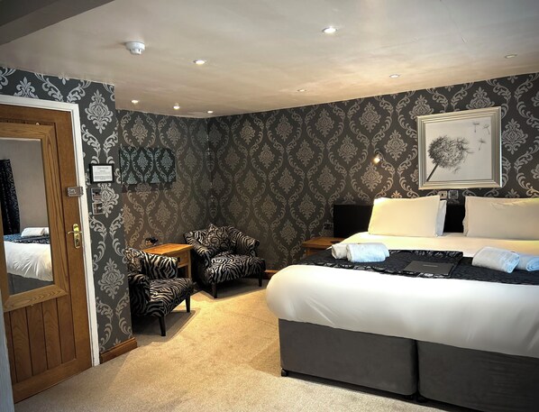Une chambre d’hôtel avec un lit, un fauteuil à motifs zébrés, une petite table et un mur orné d’un motif décoratif.
