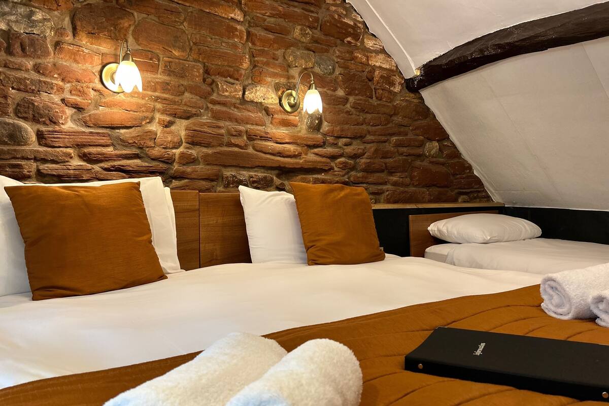 A hotel room with a stone wall, a wooden ceiling, and a bed with white and brown bedding.