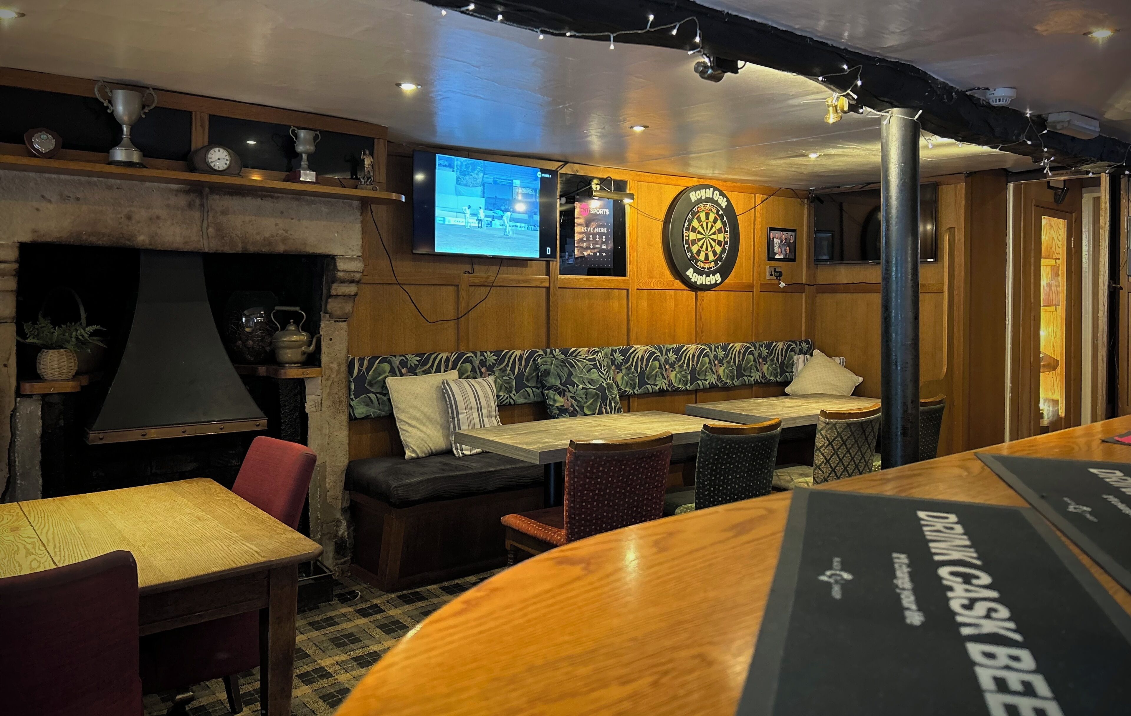 A cozy bar area with a dartboard, television screens, and a fireplace.