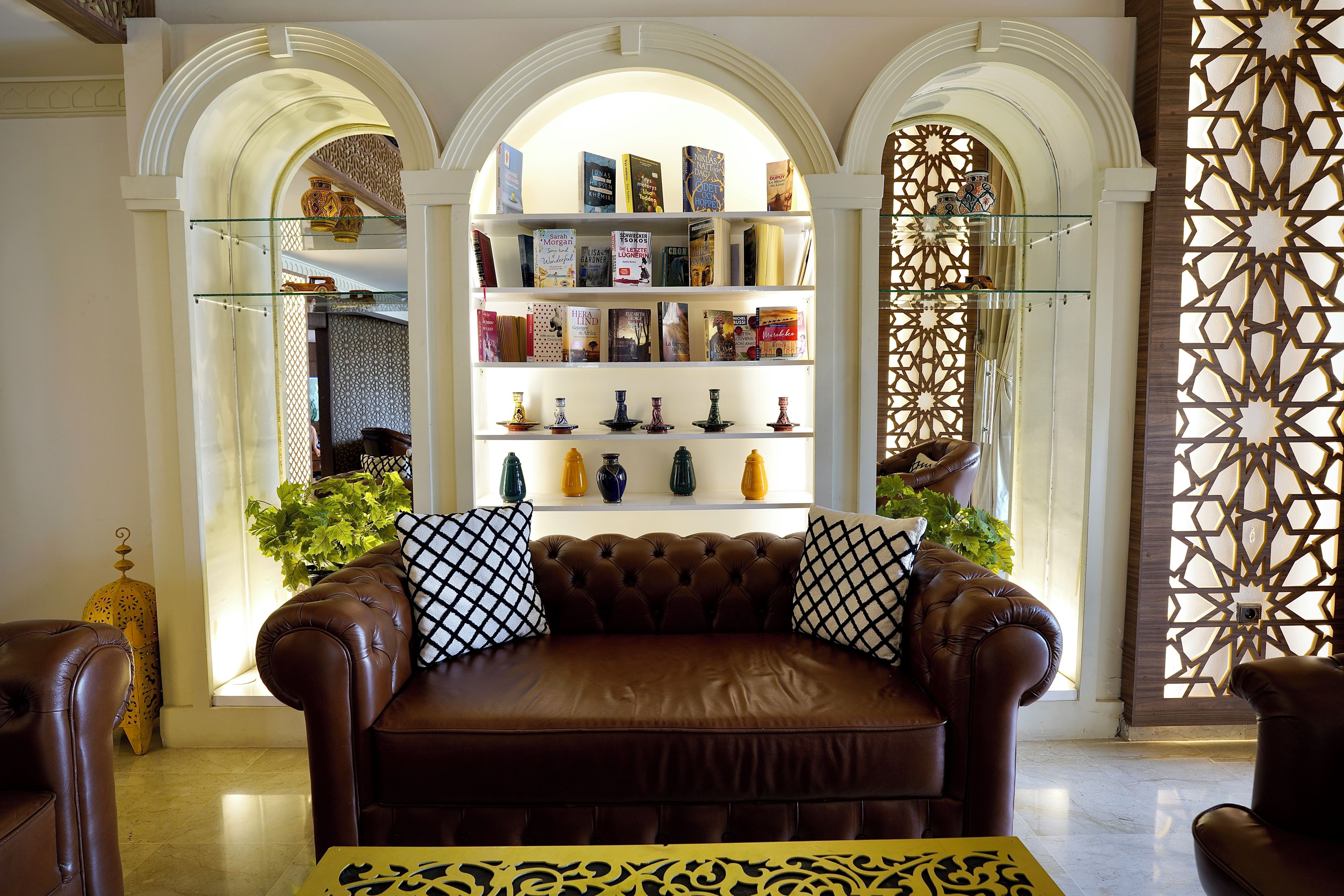 A brown leather sofa with patterned cushions, a bookshelf with various books, and decorative vases.
