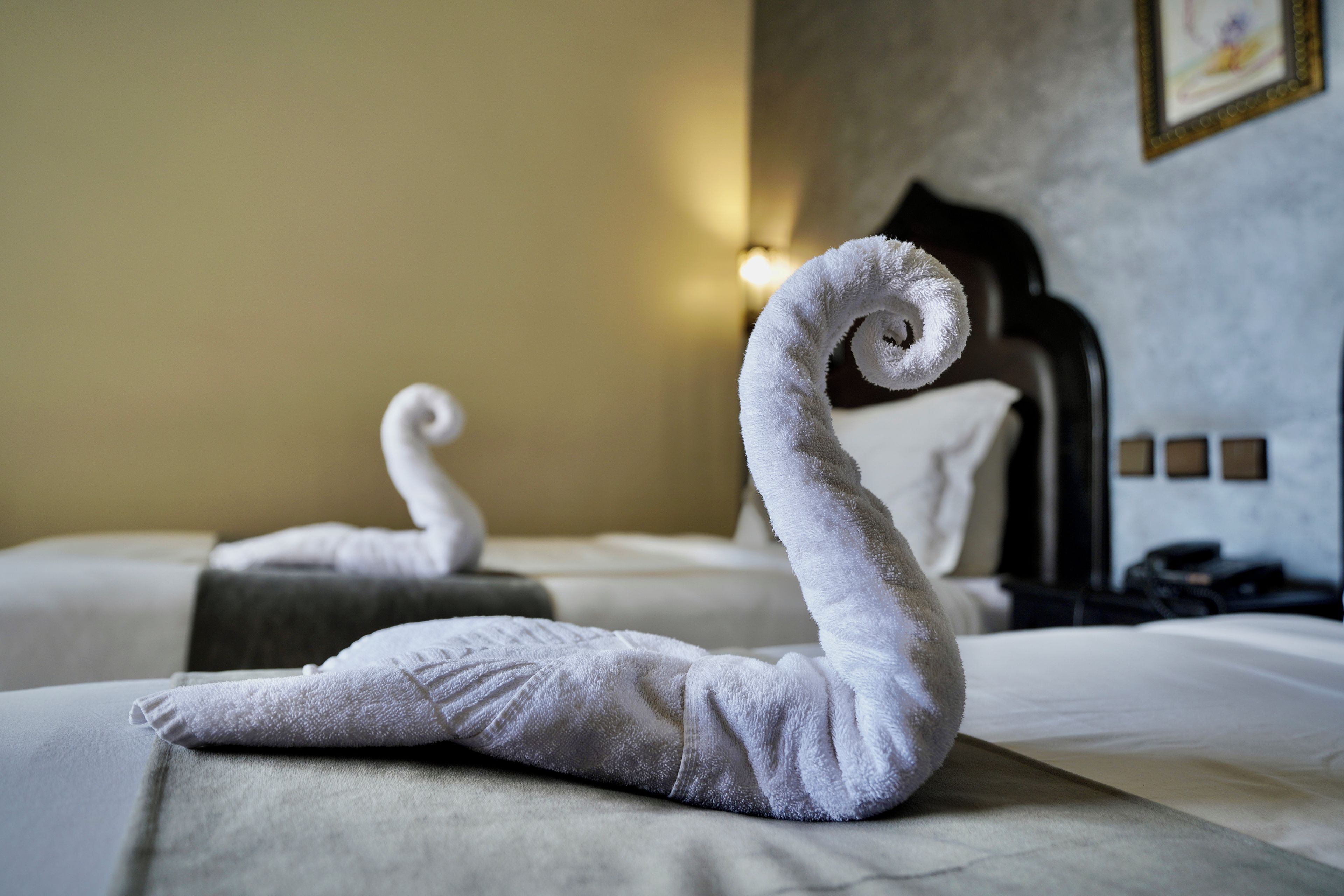 Two neatly made swan-shaped towels on a bed in a hotel room.