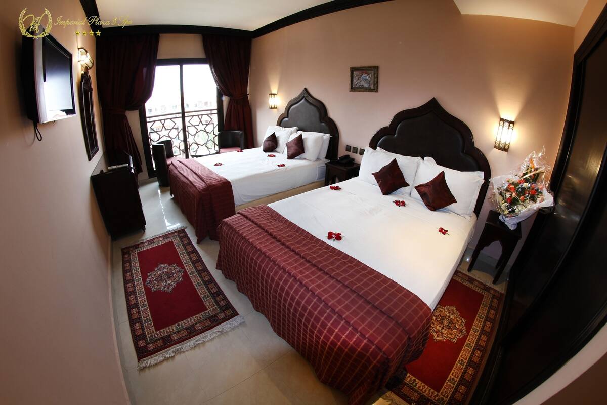 Habitación de hotel con dos camas, televisión, escritorio y ventana con cortinas.