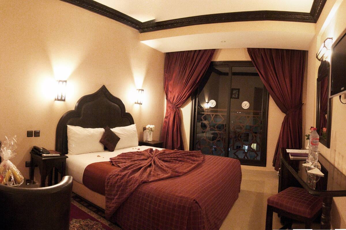 Habitación de hotel con una cama grande, un escritorio, una silla, un televisor y una ventana con cortinas.