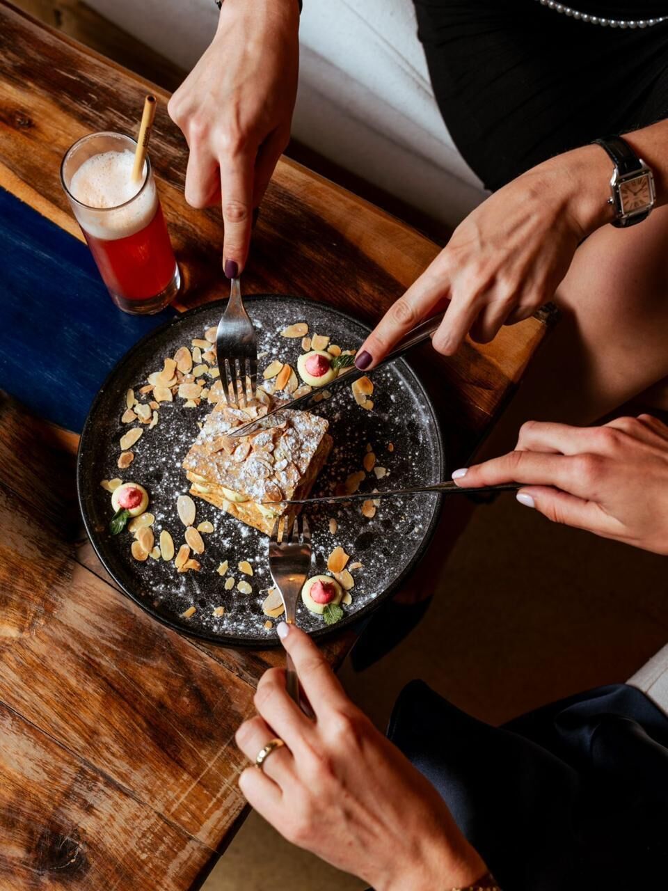 Una persona che taglia una torta su un piatto con mandorle e una spolverata di zucchero a velo.