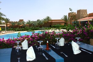 Una mesa de comedor lista para una comida, con vista a una piscina y un edificio que recuerda a un castillo al fondo.