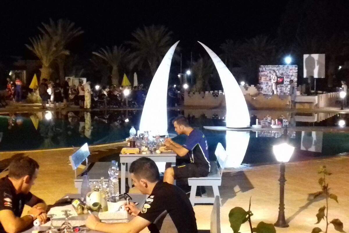 An outdoor dining area with tables and chairs, a pool, and decorative elements like a large white sculpture.