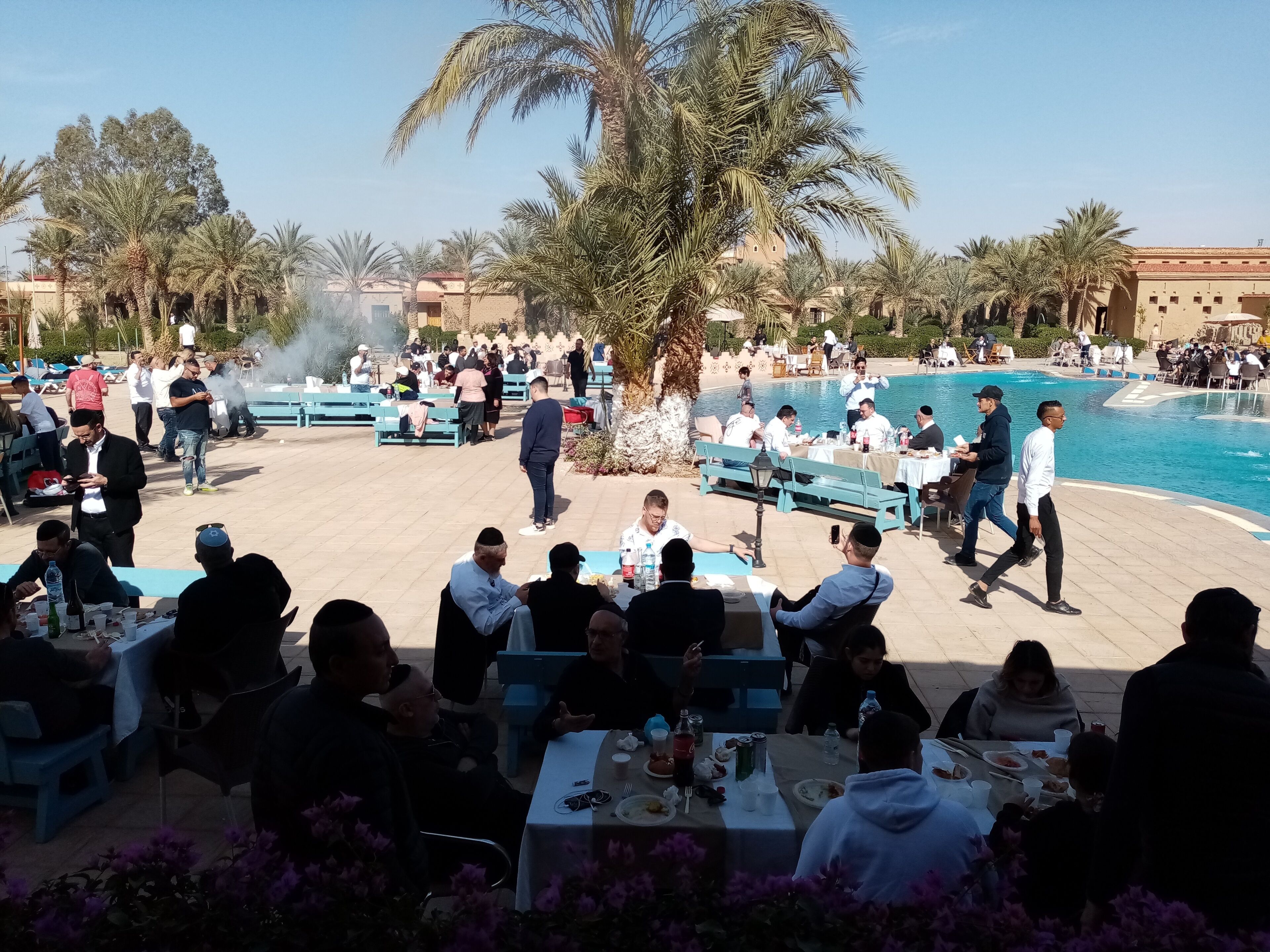 Ein Außenbereich zum Essen mit Tischen und Stühlen, ein Pool und Palmen.