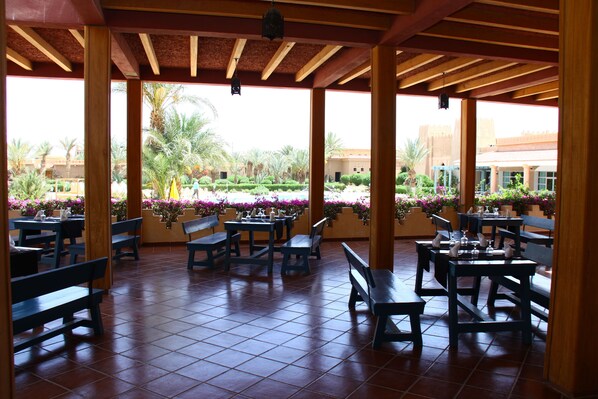 Une terrasse extérieure avec des bancs et des tables en bois, entourée de plantes et de fleurs en pot.