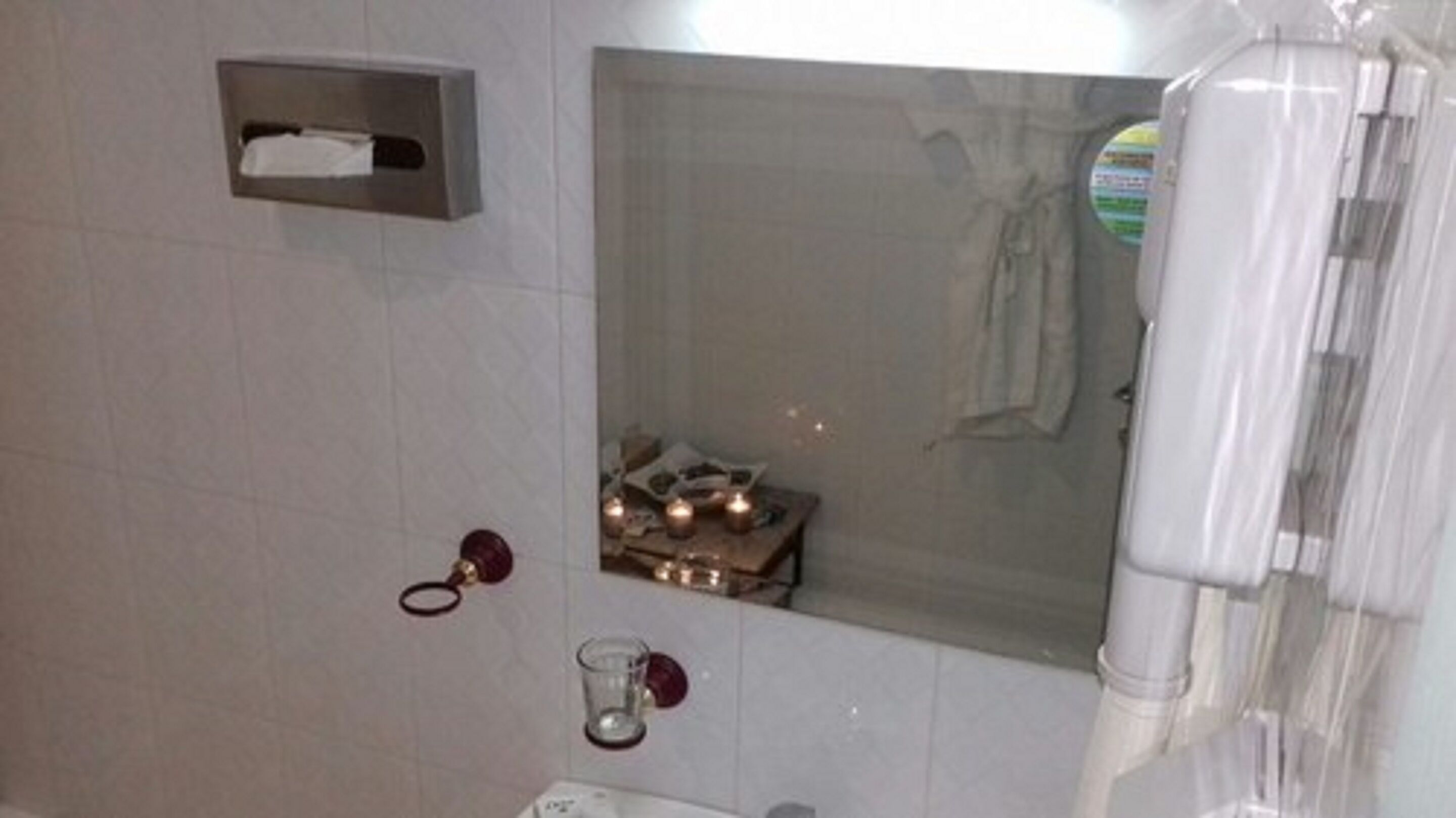 A bathroom with a mirror, a towel rack, a tissue box, and a small table with candles.