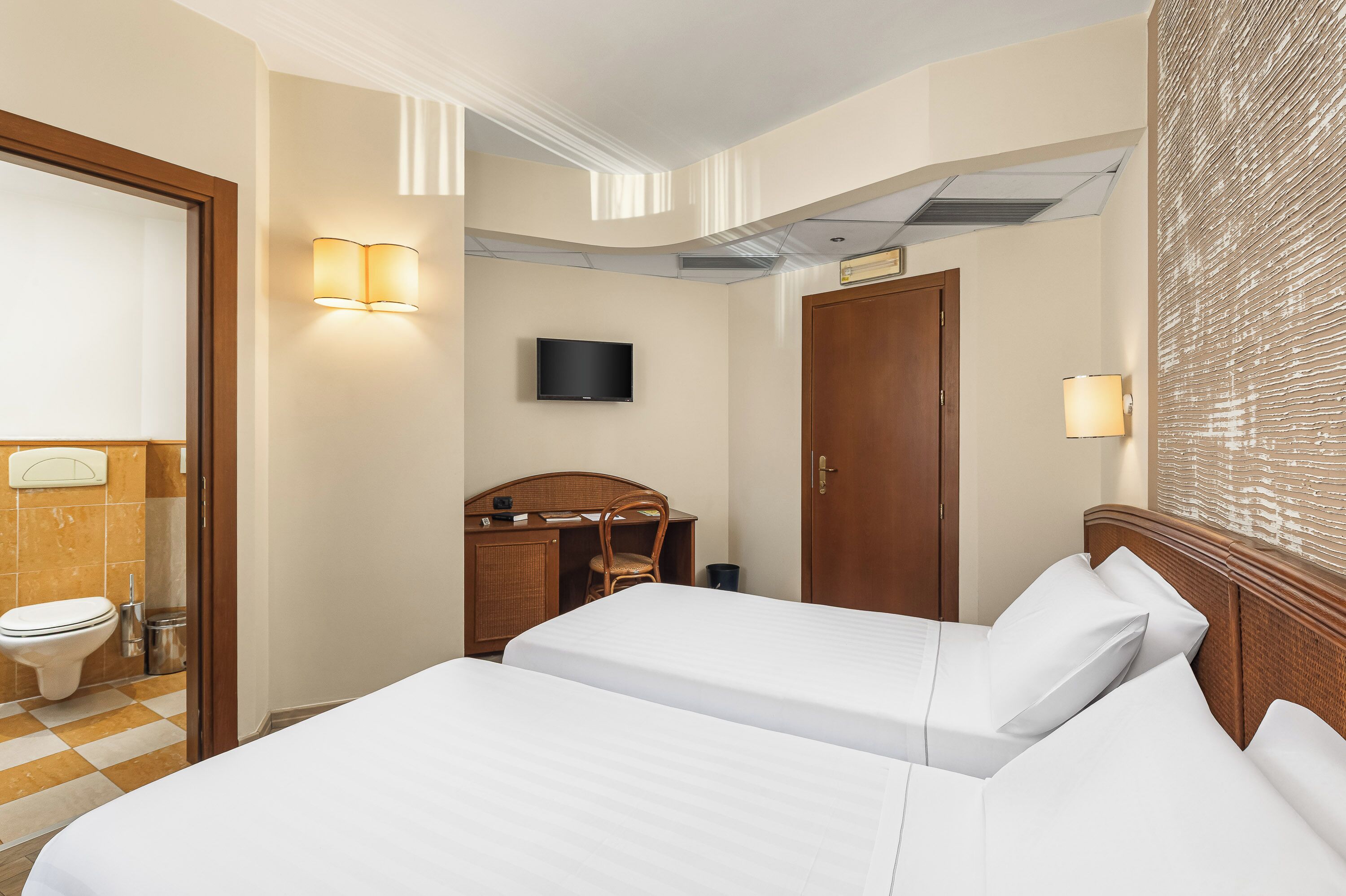 Habitació d'hotel amb dos llits, una taula de treball, televisió i bany.