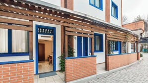 A modern building with a brick facade, blue-framed windows, and a covered entrance area. - Welcome Hotel Legnano (Legnano)
