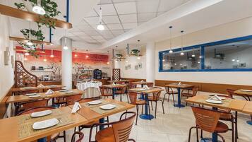 A restaurant with wooden tables and chairs, hanging plants, and a red wall with a tree mural.