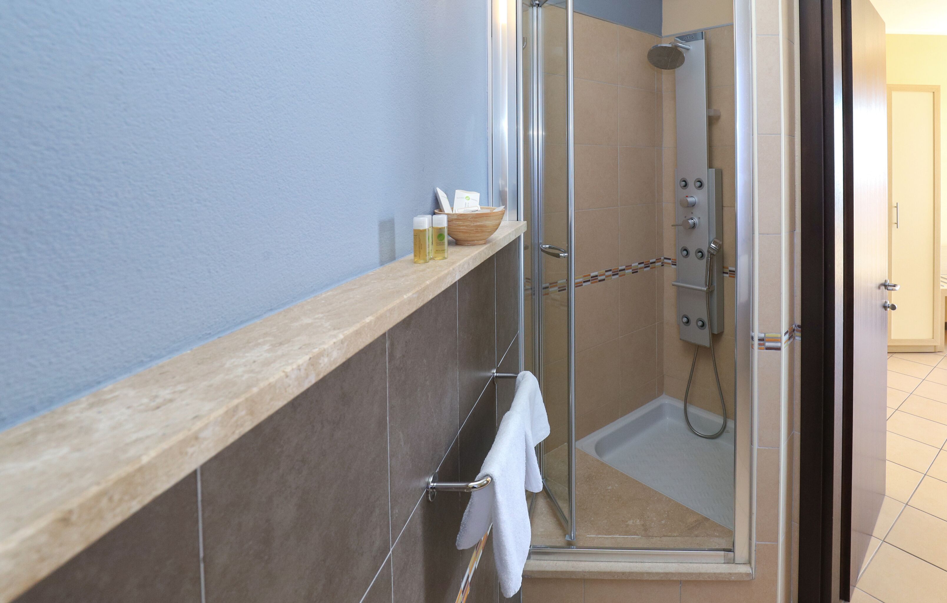 Een moderne badkamer met een douche met glazen wand, een houten plankje met toiletartikelen en een handdoekhouder.