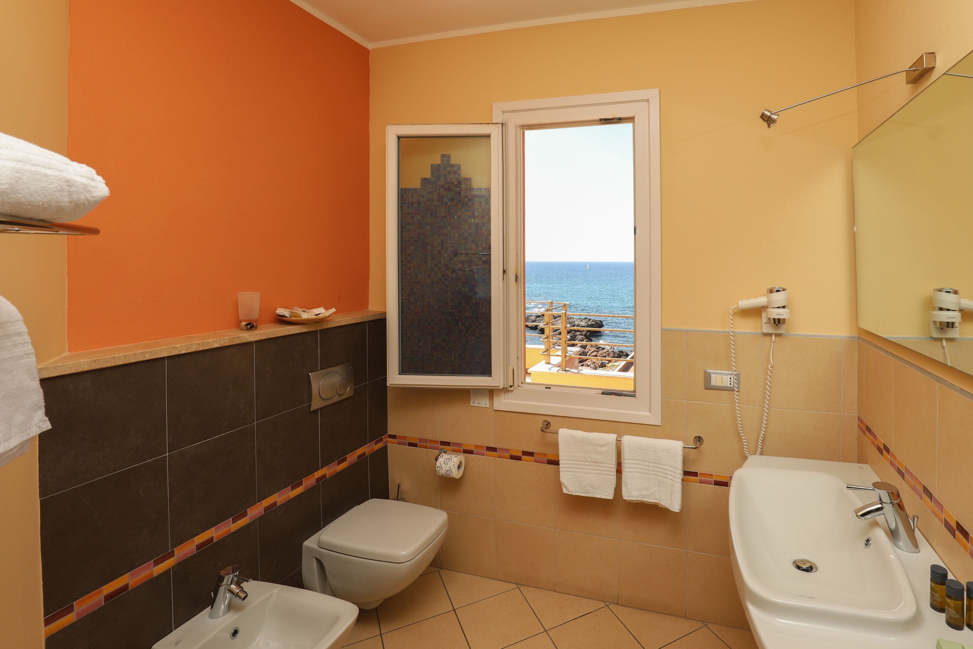 A bathroom with a toilet, sink, and bathtub. There is a window with a view of the sea.