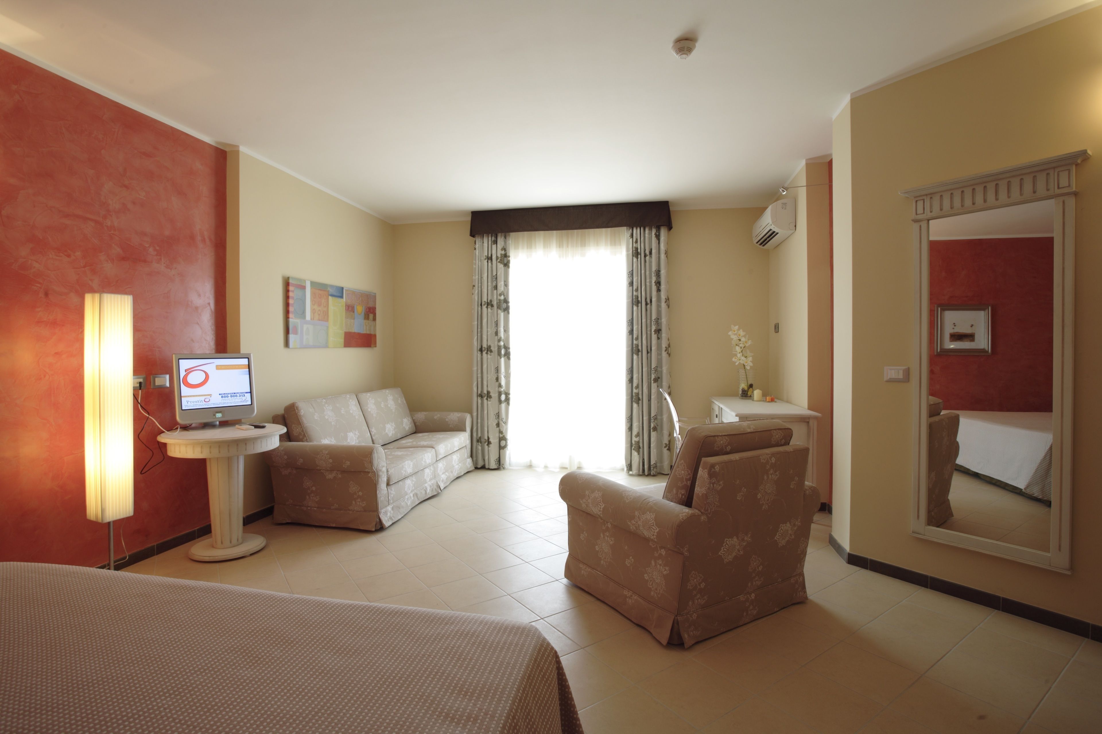 A hotel room with a bed, two sofas, a small table, a TV, and a large mirror.