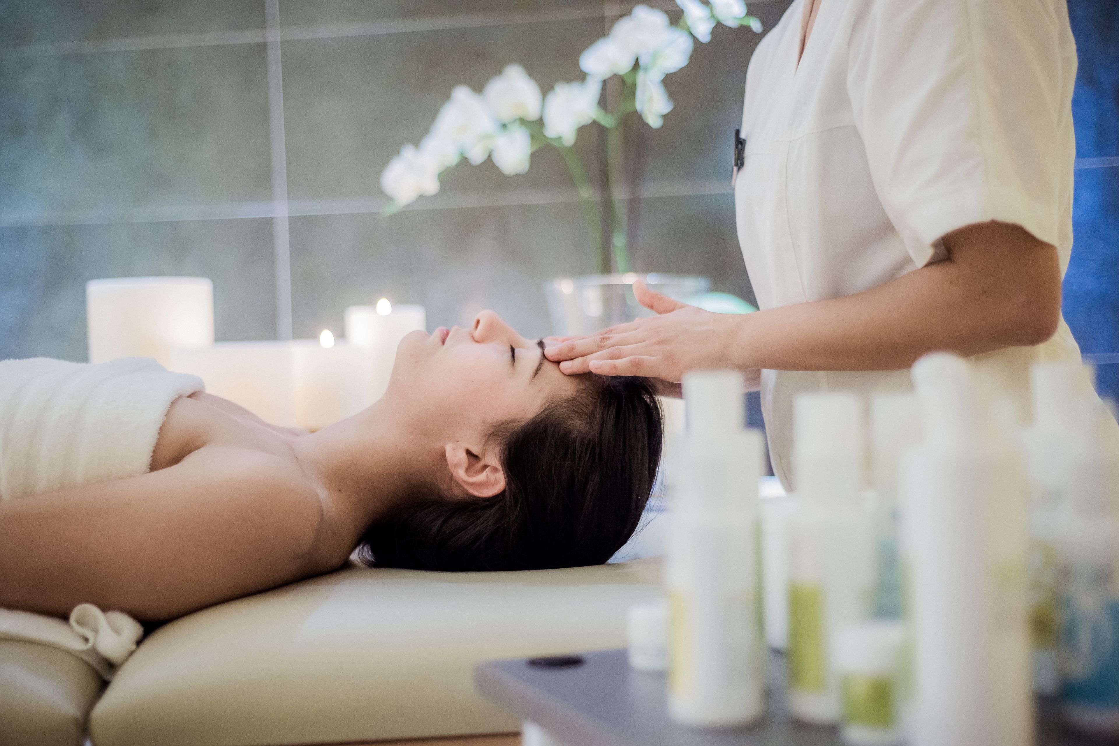 A person lying on a massage table receiving a head massage in a spa setting with candles and bottles of oils.