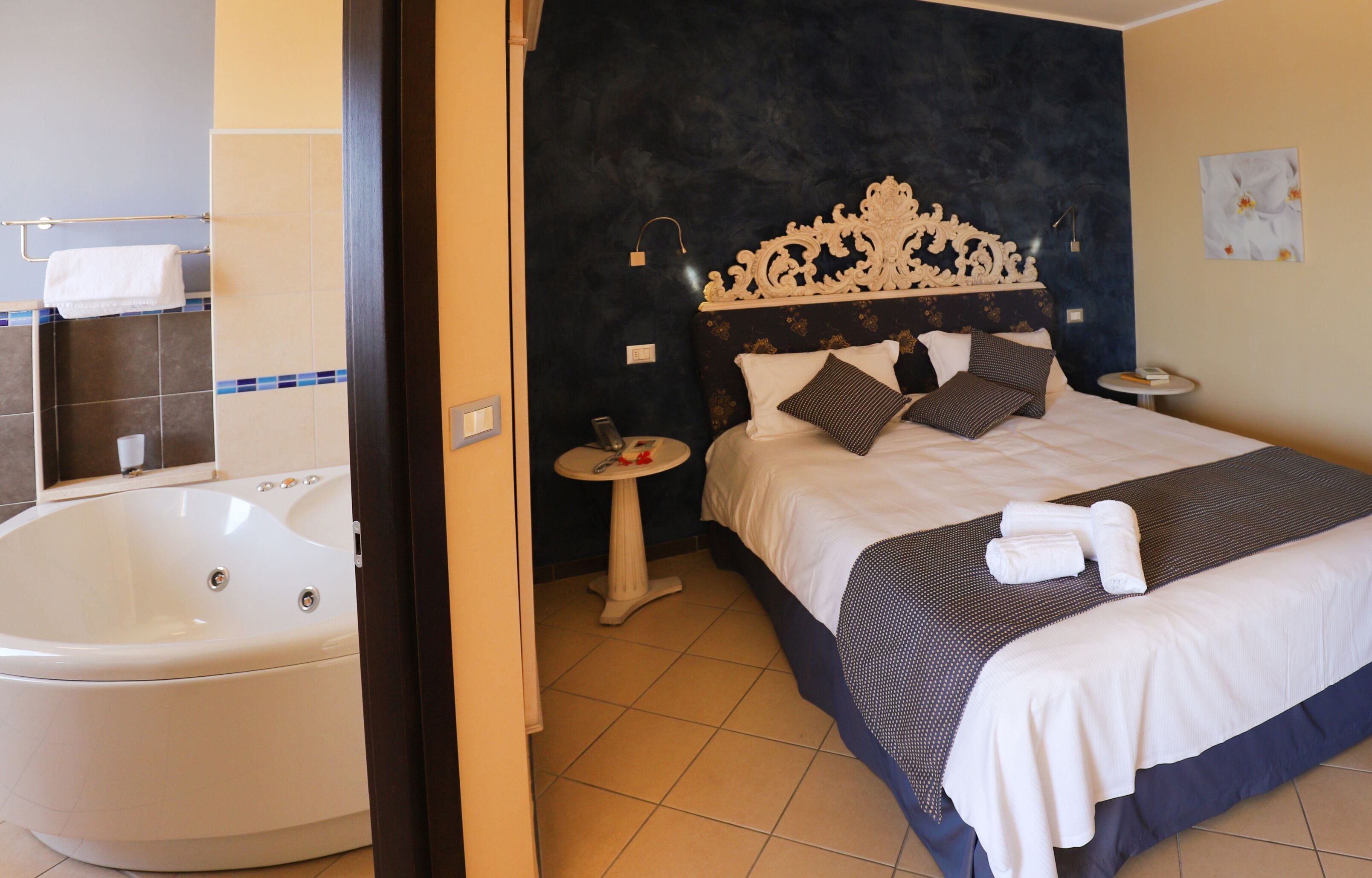 Ein Hotelzimmer mit einem großen Bett, einem Nachttisch, einer Wandlampe und einer Badewanne.